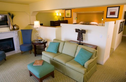 Cozy hotel suite featuring a green sofa, two chairs, a lamp, and a bed area in the background with warm lighting.