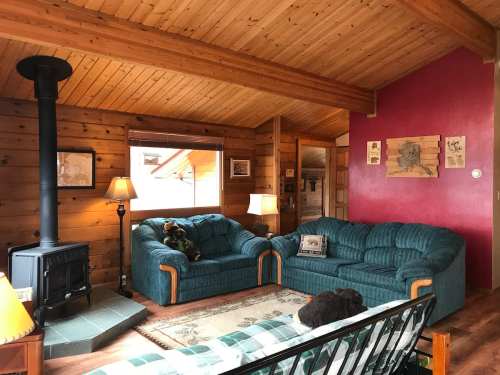 Cozy cabin interior with wooden walls, a green couch, a wood stove, and warm lighting.