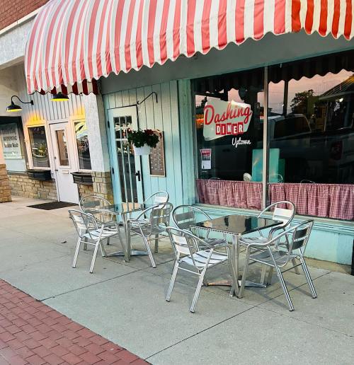 Outdoor seating area of Dashing Diner, featuring metal tables and chairs under a striped awning.