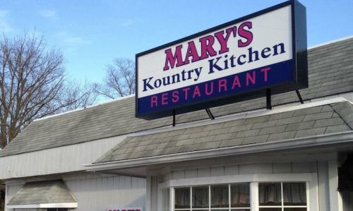 Sign for "Mary's Kountry Kitchen" restaurant, featuring a blue and pink color scheme against a gray building.