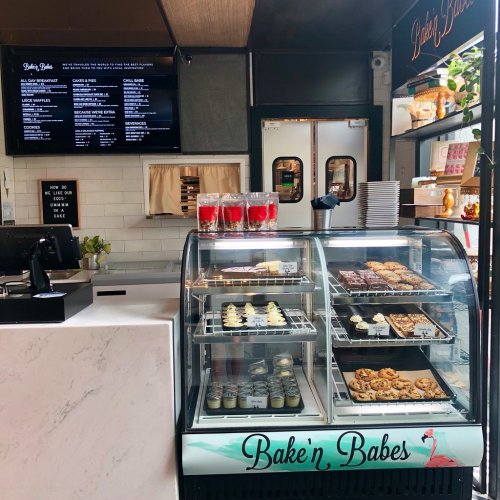 A bakery display case filled with various baked goods, with a menu board and a cash register in the background.