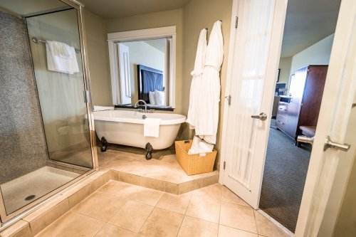 A modern bathroom featuring a shower, freestanding bathtub, and a plush robe hanging on the door.