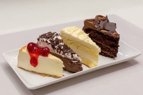 A plate with three slices of cake: chocolate, vanilla, and cheesecake topped with cherries and chocolate shavings.