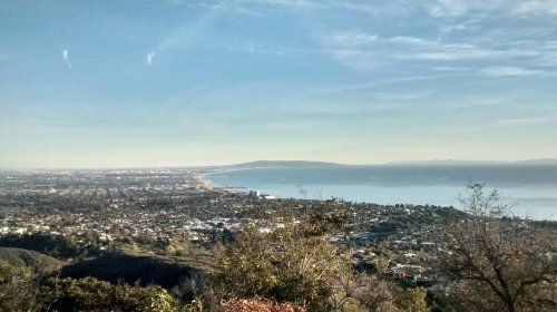 A panoramic view of a coastal city with mountains, ocean, and a clear blue sky in the background.