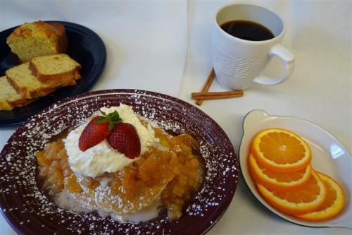 A plate of pancakes topped with strawberries, a side of sliced bread, and a cup of coffee on a table.