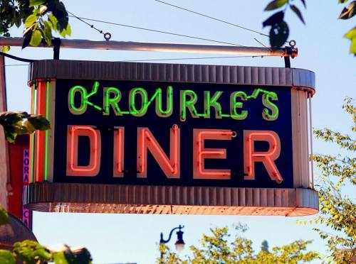 Neon sign for O'Rourke's Diner, featuring bright green and pink letters against a blue sky.