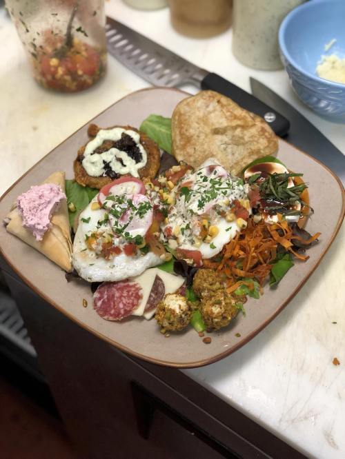 A colorful plate of food featuring eggs, vegetables, tortillas, and a side of dessert, arranged on a rustic dish.
