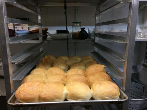 A tray of freshly baked golden rolls cooling on a rack in a kitchen.