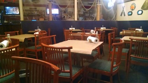 Empty restaurant with wooden tables and chairs, covered in brown paper, and a nautical-themed decor.