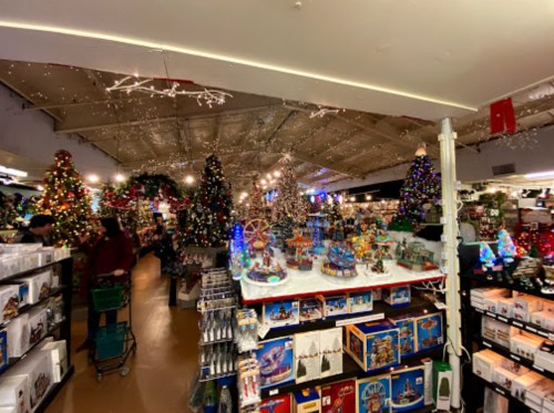 A festive store filled with Christmas trees, decorations, and holiday displays, bustling with shoppers.