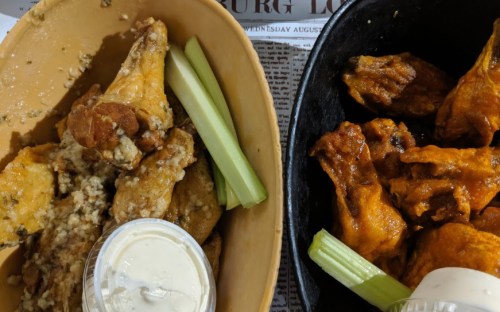 Two bowls of chicken wings: one with garlic sauce and celery, the other with buffalo sauce and celery, served with ranch dressing.