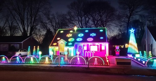 A brightly lit house decorated with colorful Christmas lights, featuring trees, snowflakes, and a Santa figure.