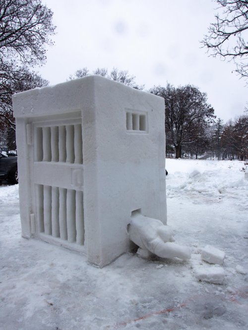 A large snow sculpture resembling a jail cell with bars and a figure reaching out from a small opening.