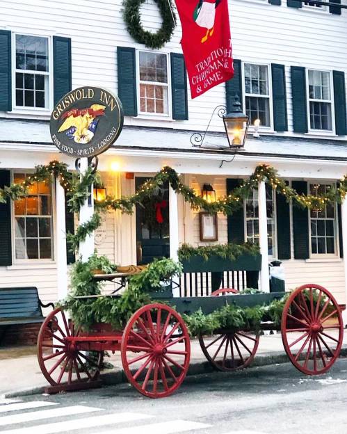A festive inn with a decorated wagon, garlands, and a holiday wreath, set against a charming building.