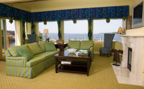 Cozy living room with striped green and blue furniture, a coffee table, and a view of a marina through large windows.
