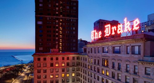 The Drake Hotel illuminated at dusk, with a view of the lake and city skyline in the background.