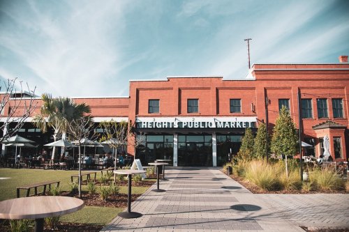 Exterior of Heights Public Market, featuring a brick building, outdoor seating, and landscaped greenery under a blue sky.