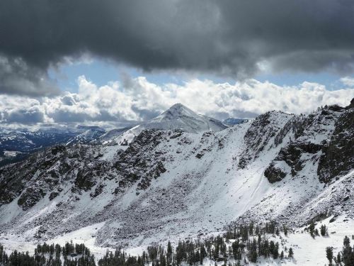 Snow-covered mountains under a dramatic sky with dark clouds and patches of blue peeking through.