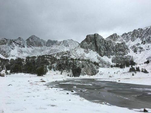 Snow-covered mountains rise above a frozen lake, under a cloudy sky, creating a serene winter landscape.