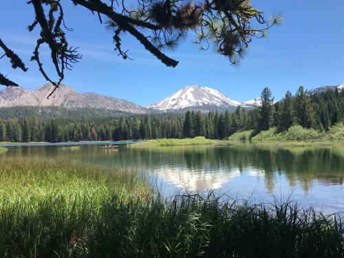 A serene lake surrounded by lush greenery and mountains, with snow-capped peaks reflecting in the water.