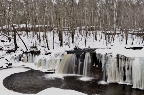 A serene winter scene featuring a waterfall surrounded by snow-covered trees and icy formations.