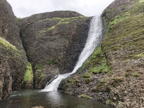 A waterfall cascading down rocky cliffs into a serene pool, surrounded by lush green vegetation.