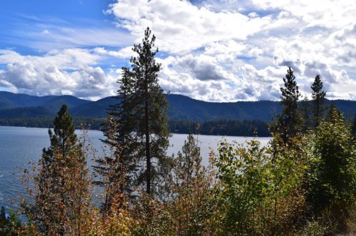 A serene lake surrounded by tall trees and mountains under a partly cloudy sky.
