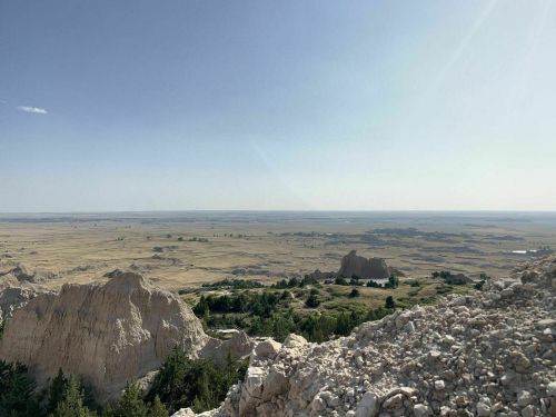 A panoramic view of a vast, open landscape with rocky formations and distant hills under a clear blue sky.