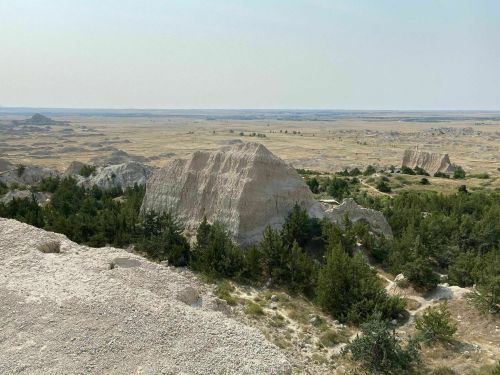 A panoramic view of rugged terrain with rocky formations and sparse greenery under a clear sky.
