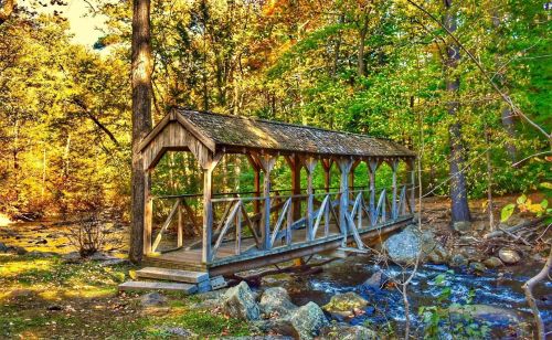 A wooden covered bridge over a stream, surrounded by vibrant autumn foliage and rocky terrain.