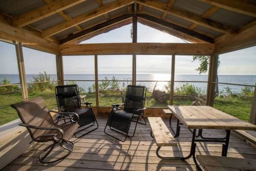 Cozy screened-in porch with two chairs and a table, overlooking a serene lake and distant horizon.