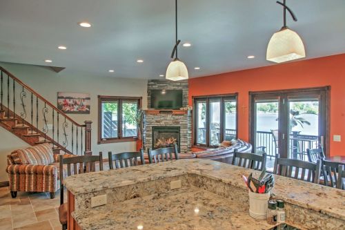 Cozy living space with a stone fireplace, large windows, and a kitchen island, overlooking a lake. Warm, inviting decor.