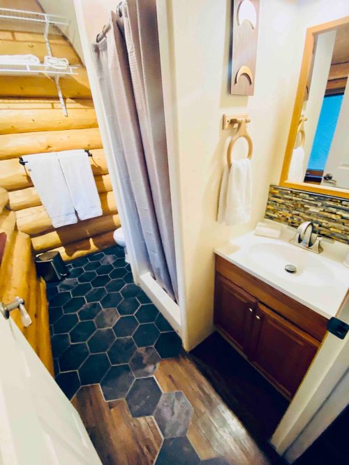 Cozy bathroom with wooden walls, a shower, sink, and hexagonal tile flooring. Towels hang neatly on hooks.