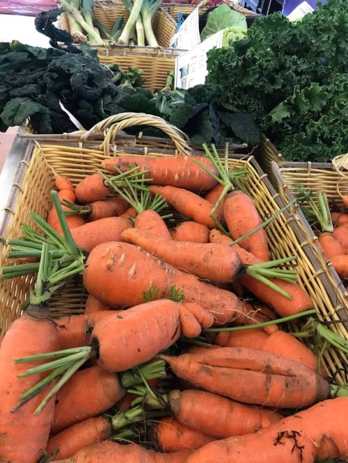 Baskets filled with fresh, vibrant orange carrots and leafy greens at a market.