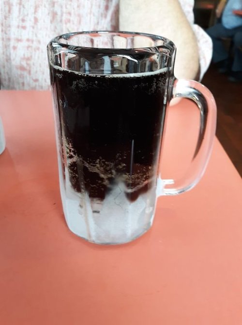 A frosty glass mug filled with dark soda, resting on a pink table.