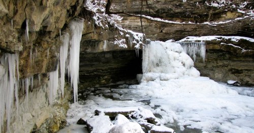 A frozen waterfall surrounded by icy rocks and snow, with icicles hanging from the cliff above.