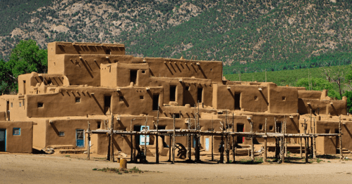 Adobe-style buildings with multiple levels, surrounded by mountains and greenery, showcasing traditional architecture.