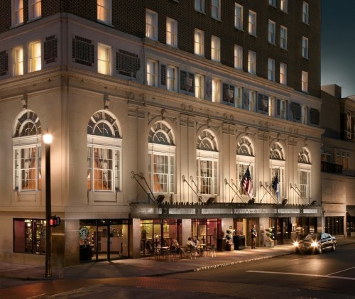 Historic hotel exterior at night, featuring elegant architecture and illuminated windows, with flags displayed.