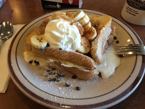 A plate of French toast topped with whipped cream, banana slices, chocolate chips, and powdered sugar.