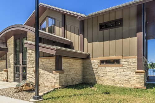 Modern building with a mix of stone and wood exterior, set against a clear blue sky and green grass.
