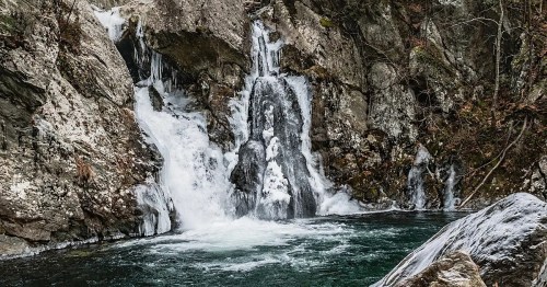 A serene waterfall cascading over rocky cliffs into a clear, tranquil pool surrounded by nature.