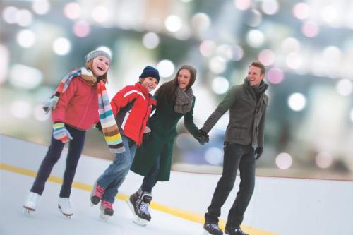 A family ice skating together, smiling and holding hands, with a blurred festive background.