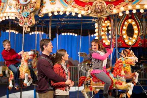 A family enjoys a carousel ride, smiling and laughing as they sit on colorful horses.