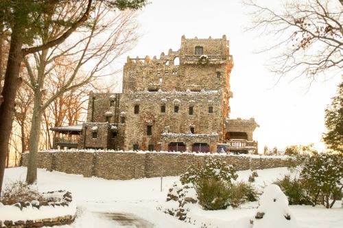 A snow-covered castle with stone walls, surrounded by trees and a winter landscape.