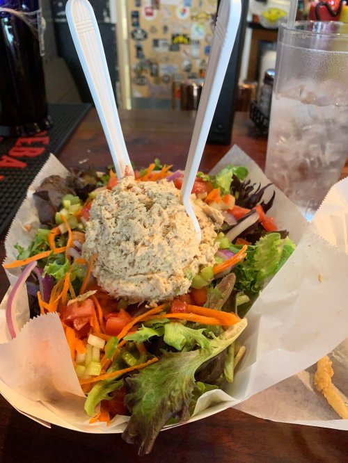 A colorful salad topped with a large scoop of tuna salad, served with two plastic forks on a wooden table.