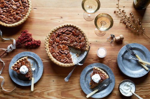 A wooden table set with pecan pie, dessert plates, glasses, and festive decorations.