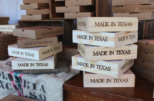 Stacked wooden boxes labeled "Made in Texas" among other packaging in a rustic setting.