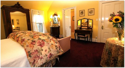Cozy bedroom with floral bedding, vintage furniture, and a vase of sunflowers on a table. Warm, inviting atmosphere.