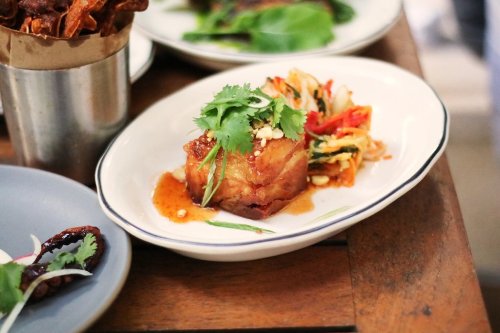 A plate of crispy pork belly topped with cilantro and served with a colorful vegetable salad on a wooden table.