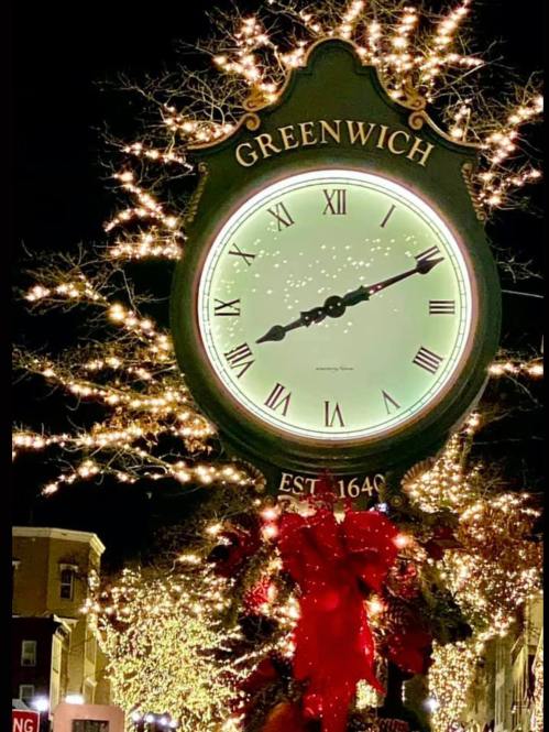 A decorative clock in Greenwich, adorned with festive lights and greenery, displaying the time at night.
